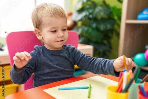 Adorable blond toddler preschool student sitting on table drawing on paper at kindergarten