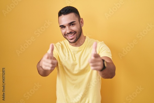 Young hispanic man standing over yellow background pointing fingers to camera with happy and funny face. good energy and vibes. © Krakenimages.com