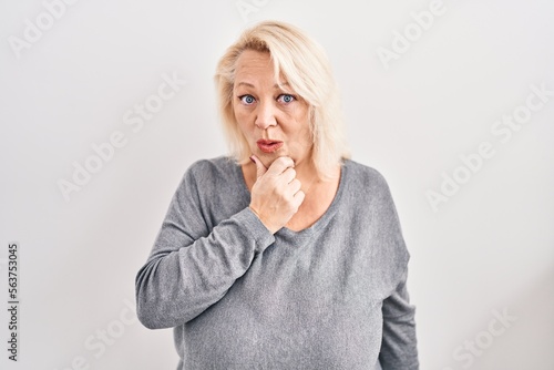 Middle age caucasian woman standing over white background looking fascinated with disbelief, surprise and amazed expression with hands on chin