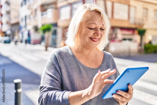 Middle age blonde woman smiling confident using touchpad at street