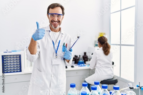 Middle age man working at scientist laboratory smiling happy and positive  thumb up doing excellent and approval sign