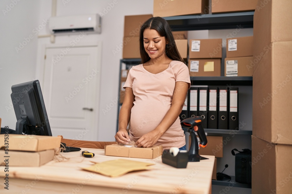 Young latin woman pregnant business worker prepare package order at office Young latin woman pregnant business worker prepare package order at office
