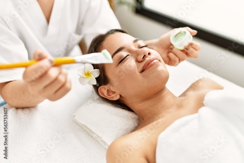 Young latin woman relaxed having skin face aloe vera treatment at beauty center