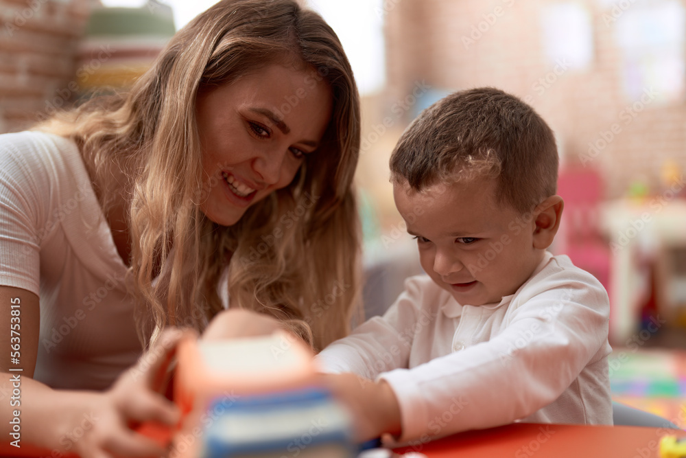 Teacher and toddler playing with cars toy sitting on table at kindergarten Teacher and toddler playing with cars toy sitting on table at kindergarten