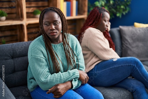African american women friends sitting on sofa with disagreement expression at home