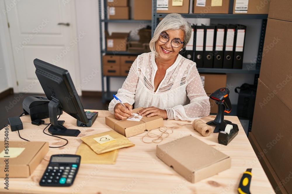 Middle age woman ecommerce business worker writing on package at office Middle age woman ecommerce business worker writing on package at office
