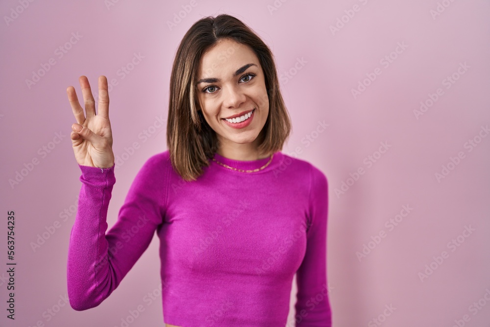 Hispanic woman standing over pink background showing and pointing up with fingers number three while smiling confident and happy. Hispanic woman standing over pink background showing and pointing up with fingers number three while smiling confident and happy.