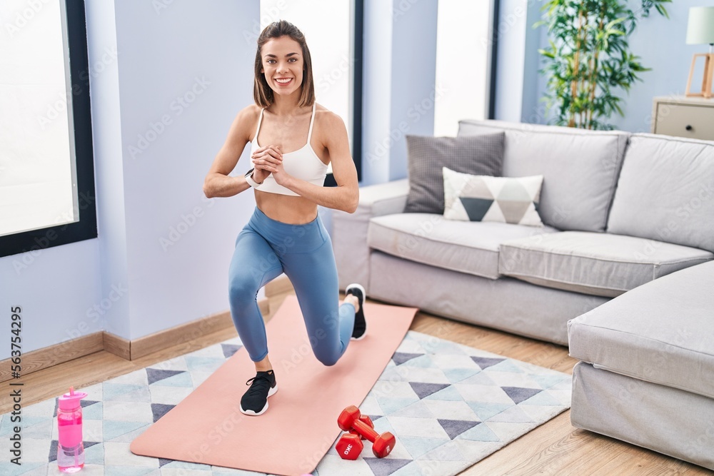 Fototapeta premium Young beautiful hispanic woman smiling confident training leg exercise at home