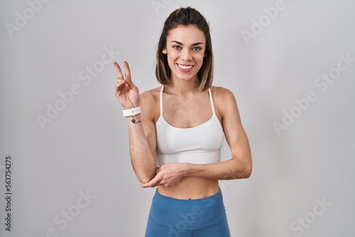 Hispanic woman wearing sportswear over isolated background smiling with happy face winking at the camera doing victory sign with fingers. number two.