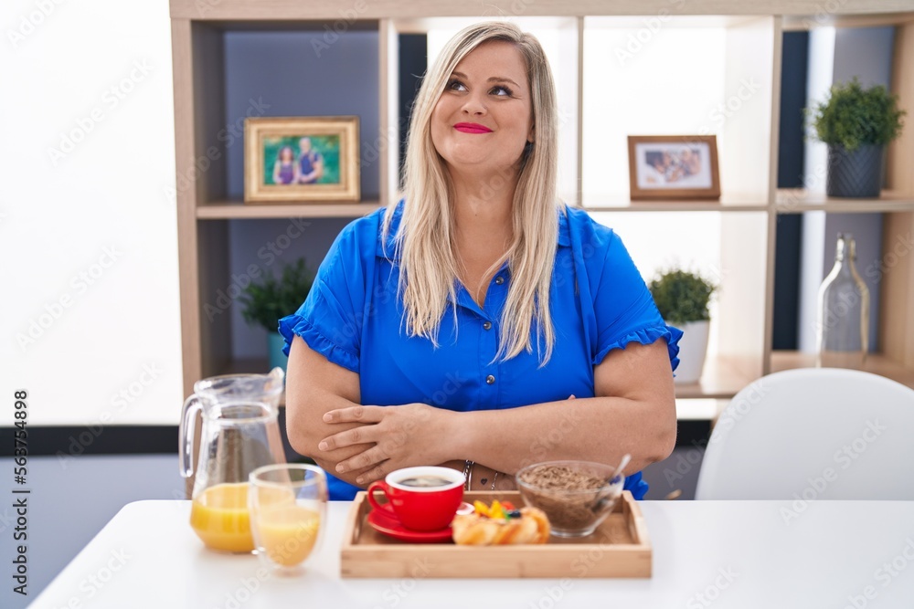 Caucasian plus size woman eating breakfast at home smiling looking to the side and staring away thinking.