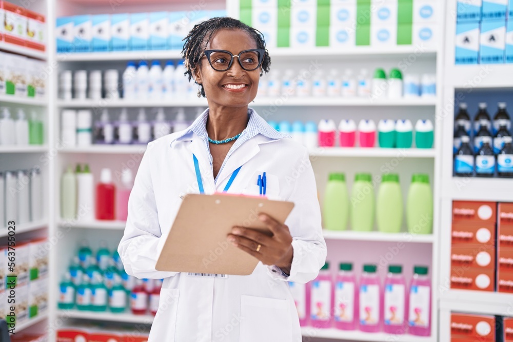 Middle age african american woman pharmacist writing on document at pharmacy Middle age african american woman pharmacist writing on document at pharmacy