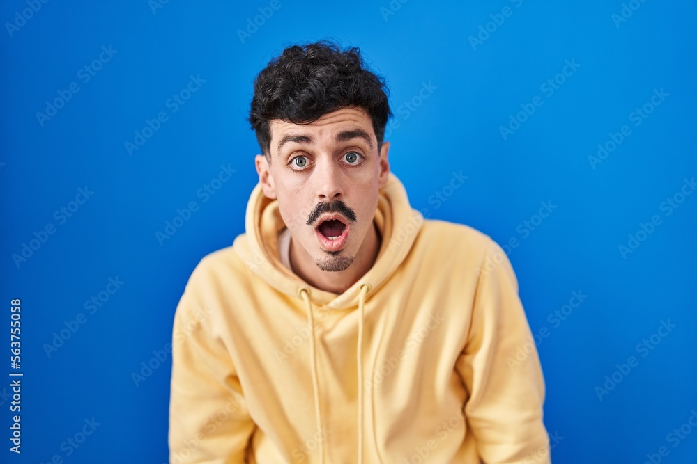 Fototapeta premium Hispanic man standing over blue background afraid and shocked with surprise and amazed expression, fear and excited face.