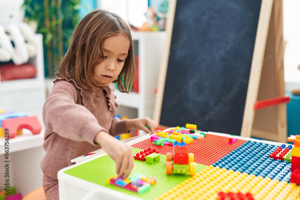 Fototapeta premium Adorable hispanic girl playing with construction blocks sitting on table at kindergarten