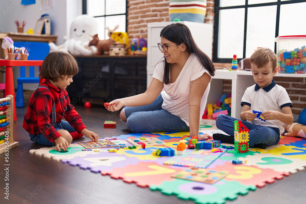 Fototapeta premium Teacher with boys playing with maths puzzle game sitting on floor at kindergarten