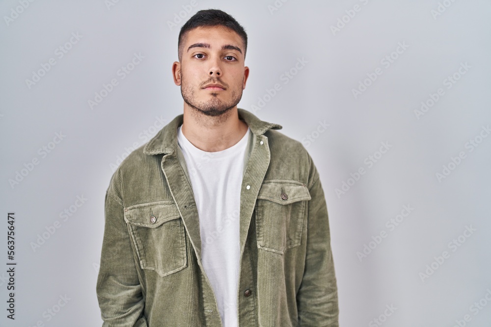 Young hispanic man standing over isolated background relaxed with serious expression on face. simple and natural looking at the camera. Young hispanic man standing over isolated background relaxed with serious expression on face. simple and natural looking at the camera.