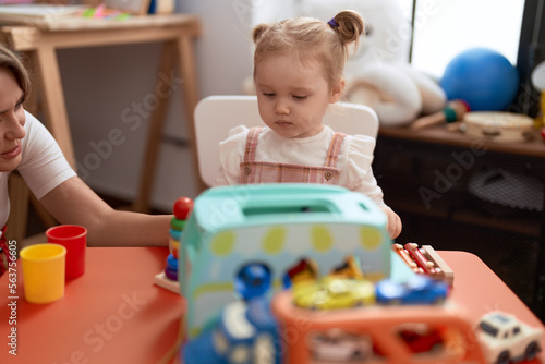 Teacher and toddler sitting on table playing with toys at kindergarten