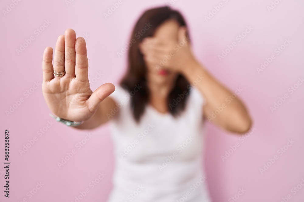 Middle age brunette woman standing over pink background covering eyes with hands and doing stop gesture with sad and fear expression. embarrassed and negative concept. Middle age brunette woman standing over pink background covering eyes with hands and doing stop gesture with sad and fear expression. embarrassed and negative concept.