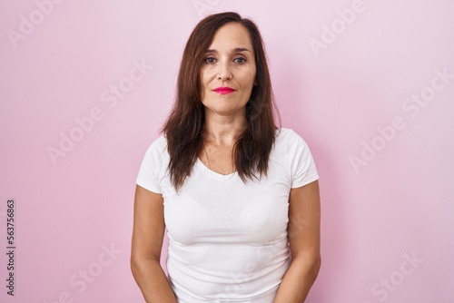 Middle age brunette woman standing over pink background relaxed with serious expression on face. simple and natural looking at the camera.