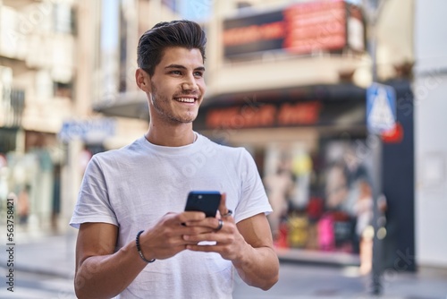 Young hispanic man smiling confident using smartphone at street