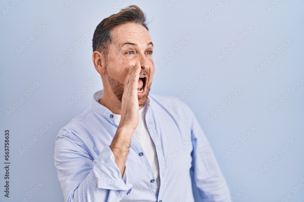 Middle age caucasian man standing over blue background shouting and screaming loud to side with hand on mouth. communication concept. Middle age caucasian man standing over blue background shouting and screaming loud to side with hand on mouth. communication concept.