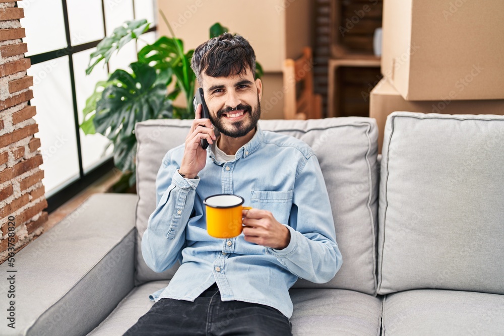 Young hispanic man talking on smartphone drinking coffee at new home Young hispanic man talking on smartphone drinking coffee at new home