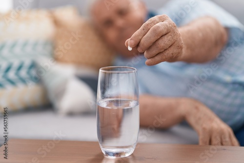 Middle age grey-haired man pouring pill on glass of water at home