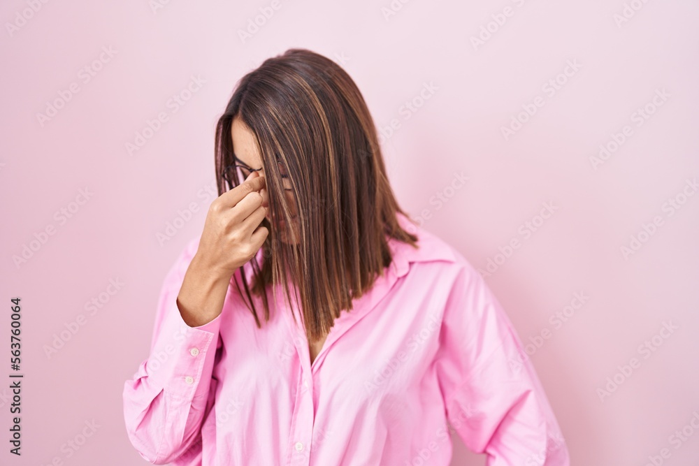 Young hispanic woman wearing glasses standing over pink background tired rubbing nose and eyes feeling fatigue and headache. stress and frustration concept. Young hispanic woman wearing glasses standing over pink background tired rubbing nose and eyes feeling fatigue and headache. stress and frustration concept.