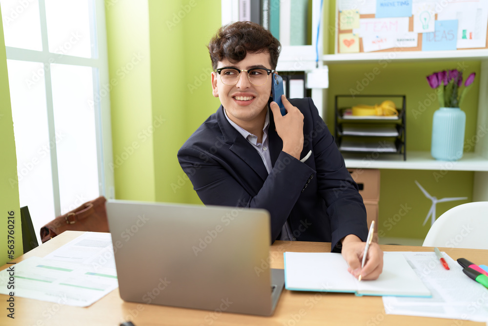 Non binary man business worker talking on smartphone writing on notebook at office Non binary man business worker talking on smartphone writing on notebook at office
