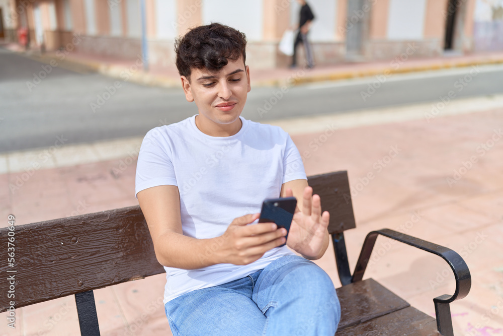 Obraz premium Non binary man using smartphone sitting on bench at park