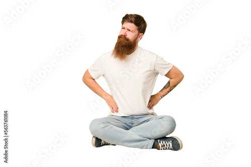 Young adult redhead with a long beard sitting on the floor isolated confused, feels doubtful and unsure.