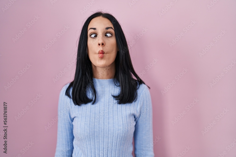 Hispanic woman standing over pink background making fish face with lips, crazy and comical gesture. funny expression. Hispanic woman standing over pink background making fish face with lips, crazy and comical gesture. funny expression.