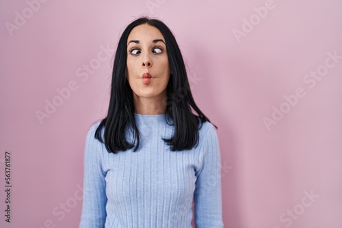 Hispanic woman standing over pink background making fish face with lips, crazy and comical gesture. funny expression.
