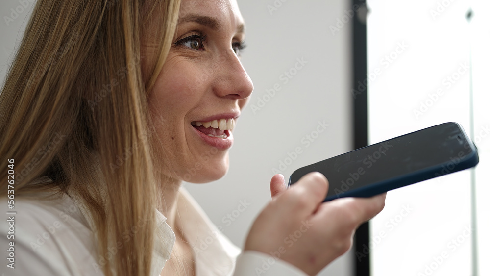 Young blonde woman sending voice message by smartphone sitting on sofa at home Young blonde woman sending voice message by smartphone sitting on sofa at home