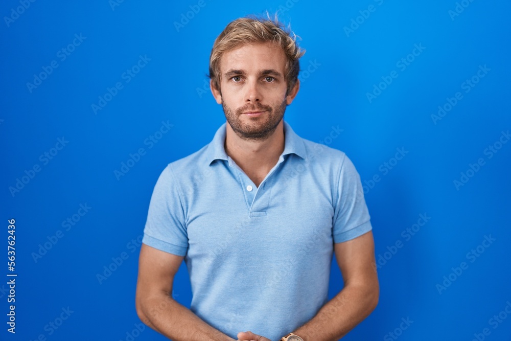 Caucasian man standing over blue background with hands together and crossed fingers smiling relaxed and cheerful. success and optimistic Caucasian man standing over blue background with hands together and crossed fingers smiling relaxed and cheerful. success and optimistic