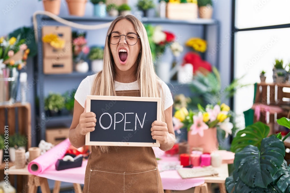Young blonde woman working at florist holding open sign angry and mad screaming frustrated and furious, shouting with anger. rage and aggressive concept. Young blonde woman working at florist holding open sign angry and mad screaming frustrated and furious, shouting with anger. rage and aggressive concept.