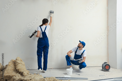 Professional workers plastering wall with putty knives indoors photo