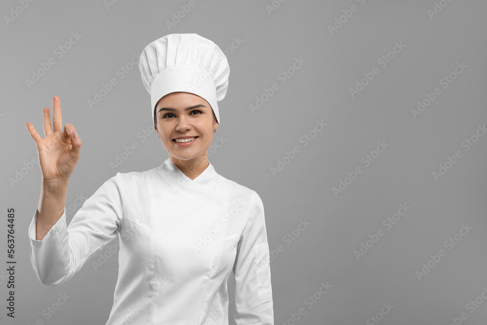 Happy female chef wearing uniform and cap showing ok gesture on light grey background. Space for text Happy female chef wearing uniform and cap showing ok gesture on light grey background. Space for text