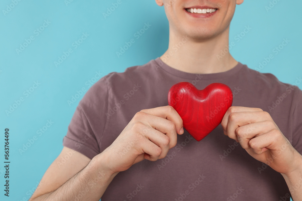 Happy volunteer holding red heart with hands on light blue background, closeup Happy volunteer holding red heart with hands on light blue background, closeup
