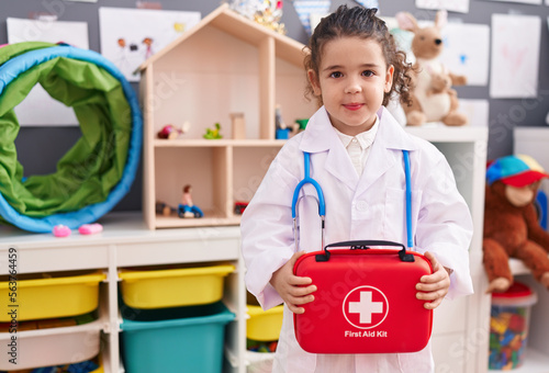 Adorable hispanic girl wearing doctor uniform holding first kit aid at kindergarten