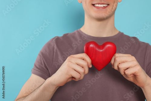Fototapeta Naklejka Na Ścianę i Meble -  Happy volunteer holding red heart with hands on light blue background, closeup