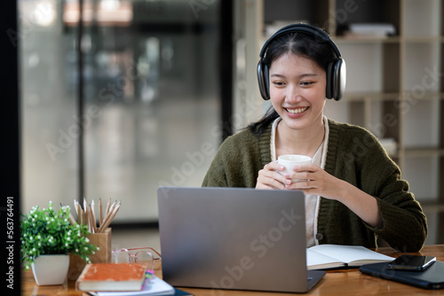 Young attractive university student with headphone using laptop computer, studying at modern library. Cheerful caucasian woman learning online at home.