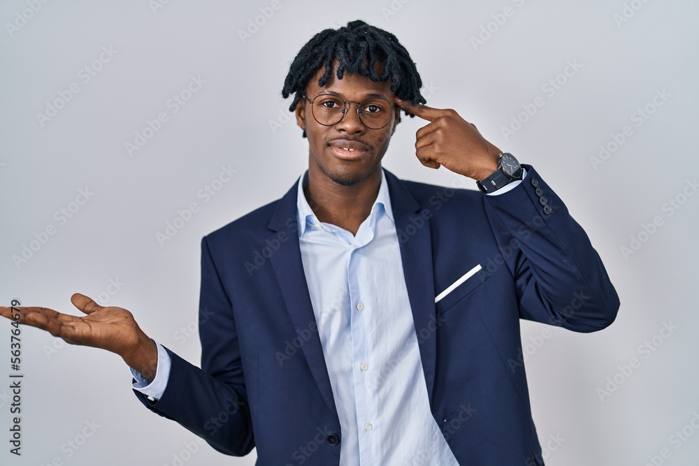 Young african man with dreadlocks wearing business jacket over white background confused and annoyed with open palm showing copy space and pointing finger to forehead. think about it. Young african man with dreadlocks wearing business jacket over white background confused and annoyed with open palm showing copy space and pointing finger to forehead. think about it.