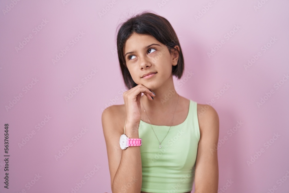 Young girl standing over pink background with hand on chin thinking about question, pensive expression. smiling with thoughtful face. doubt concept. Young girl standing over pink background with hand on chin thinking about question, pensive expression. smiling with thoughtful face. doubt concept.