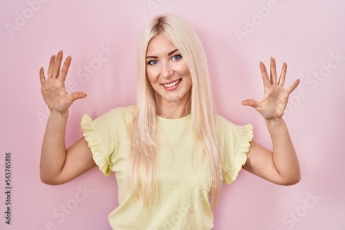 Caucasian woman standing over pink background showing and pointing up with fingers number ten while smiling confident and happy.