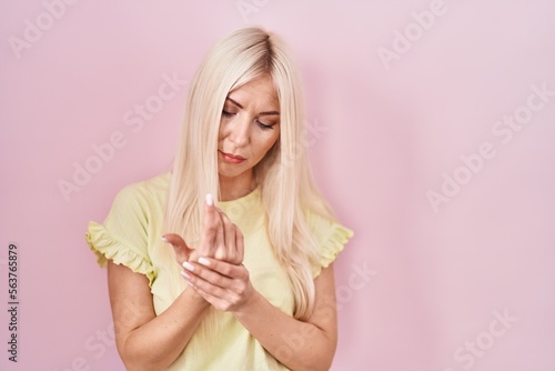 Caucasian woman standing over pink background suffering pain on hands and fingers, arthritis inflammation