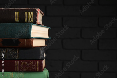 Stack of old hardcover books near black wall, closeup. Space for text