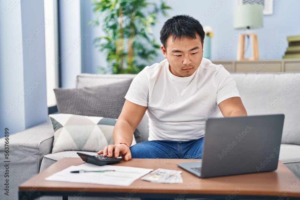 Young chinese man accounting economy using laptop and calculator at home Young chinese man accounting economy using laptop and calculator at home