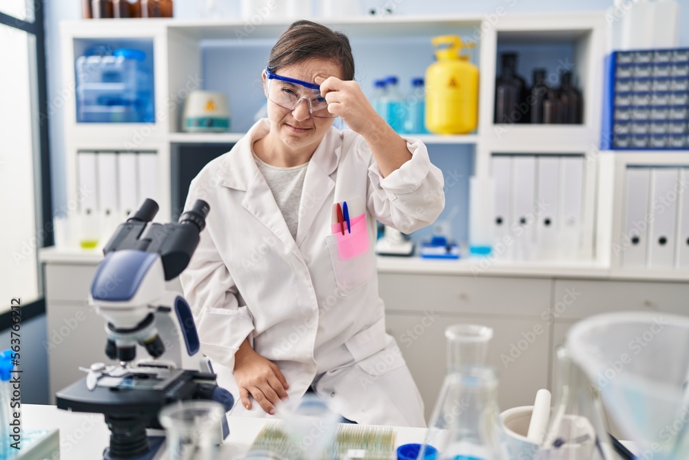 Hispanic girl with down syndrome working at scientist laboratory pointing unhappy to pimple on forehead, ugly infection of blackhead. acne and skin problem Hispanic girl with down syndrome working at scientist laboratory pointing unhappy to pimple on forehead, ugly infection of blackhead. acne and skin problem