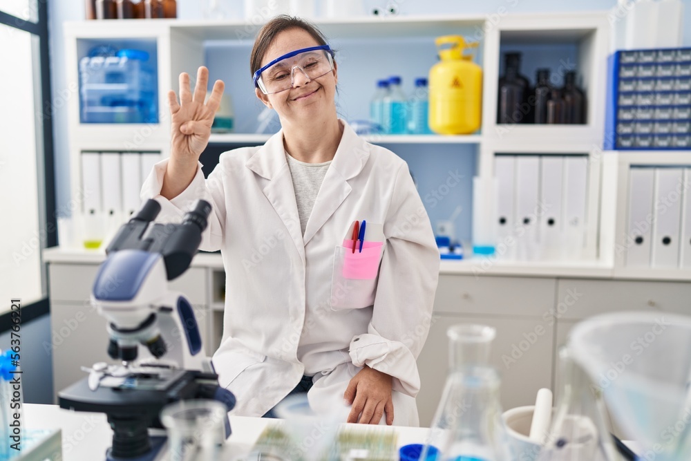 Hispanic girl with down syndrome working at scientist laboratory showing and pointing up with fingers number four while smiling confident and happy. Hispanic girl with down syndrome working at scientist laboratory showing and pointing up with fingers number four while smiling confident and happy.