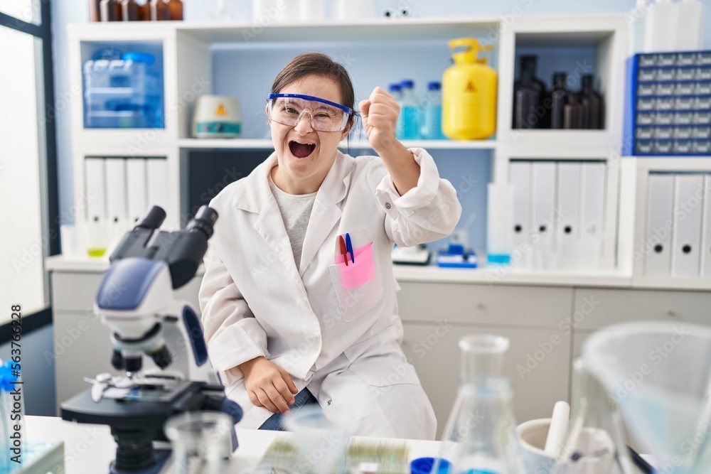 Hispanic girl with down syndrome working at scientist laboratory angry and mad raising fist frustrated and furious while shouting with anger. rage and aggressive concept. Hispanic girl with down syndrome working at scientist laboratory angry and mad raising fist frustrated and furious while shouting with anger. rage and aggressive concept.